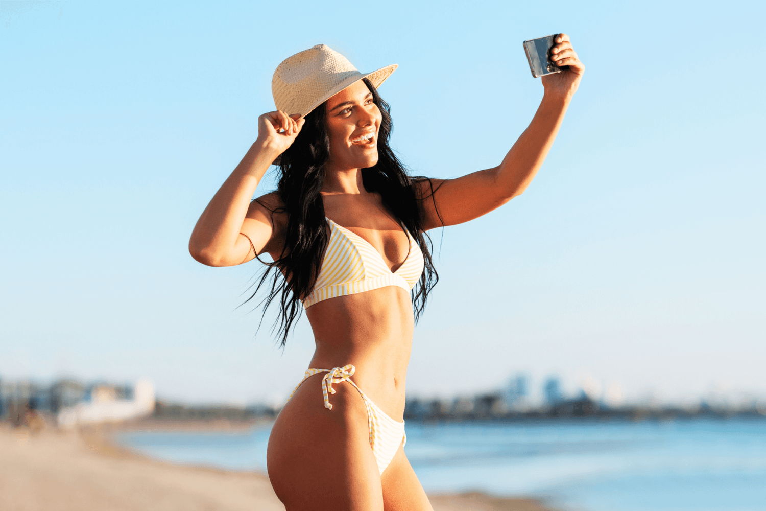 Joyful woman taking a beach selfie after Brazilian IPL hair removal.