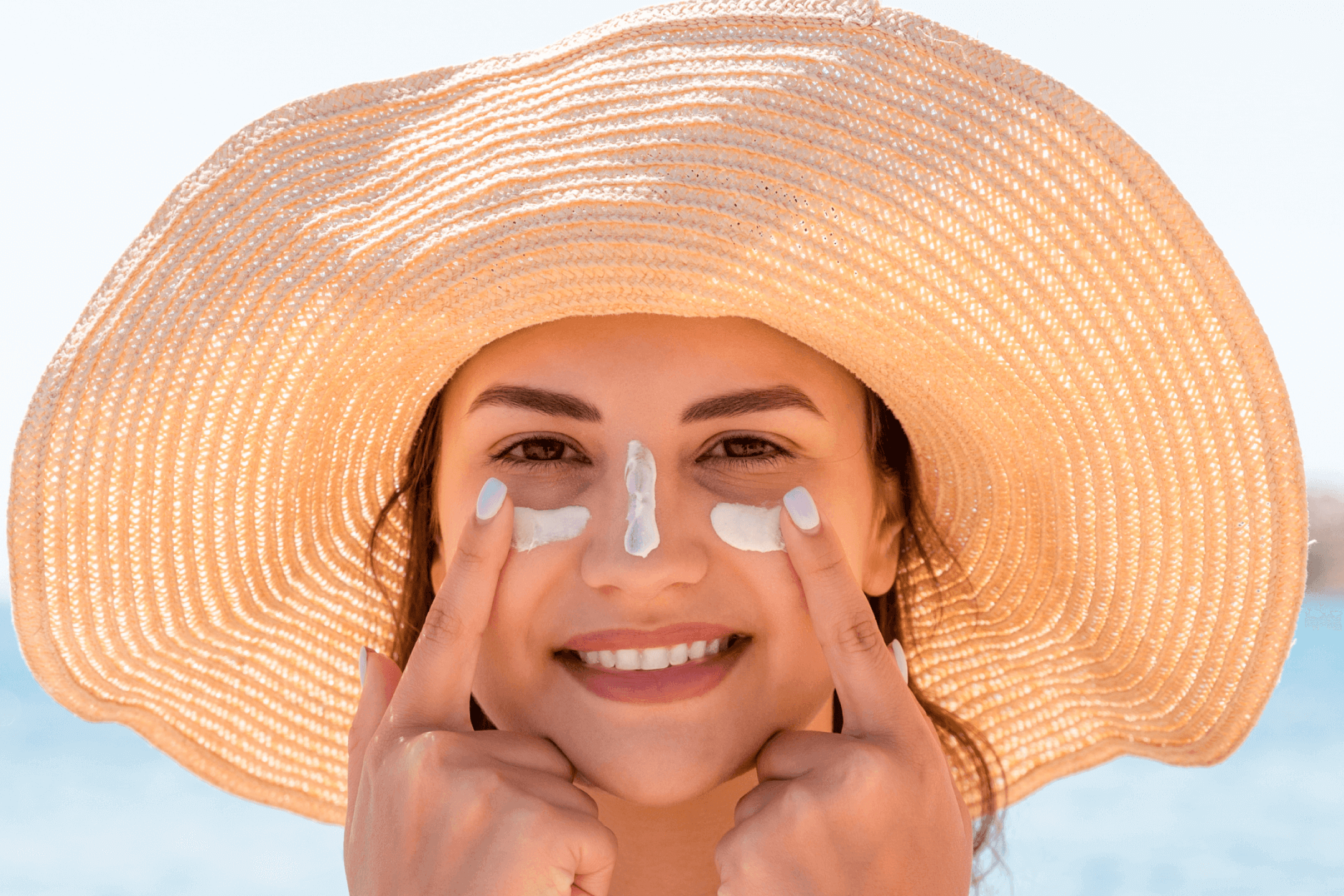 woman on the beach applying sunscreen to her face to prevent sunspots