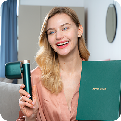 Smiling woman holding JOVS Venus II IPL hair removal device alongside its elegant green packaging.