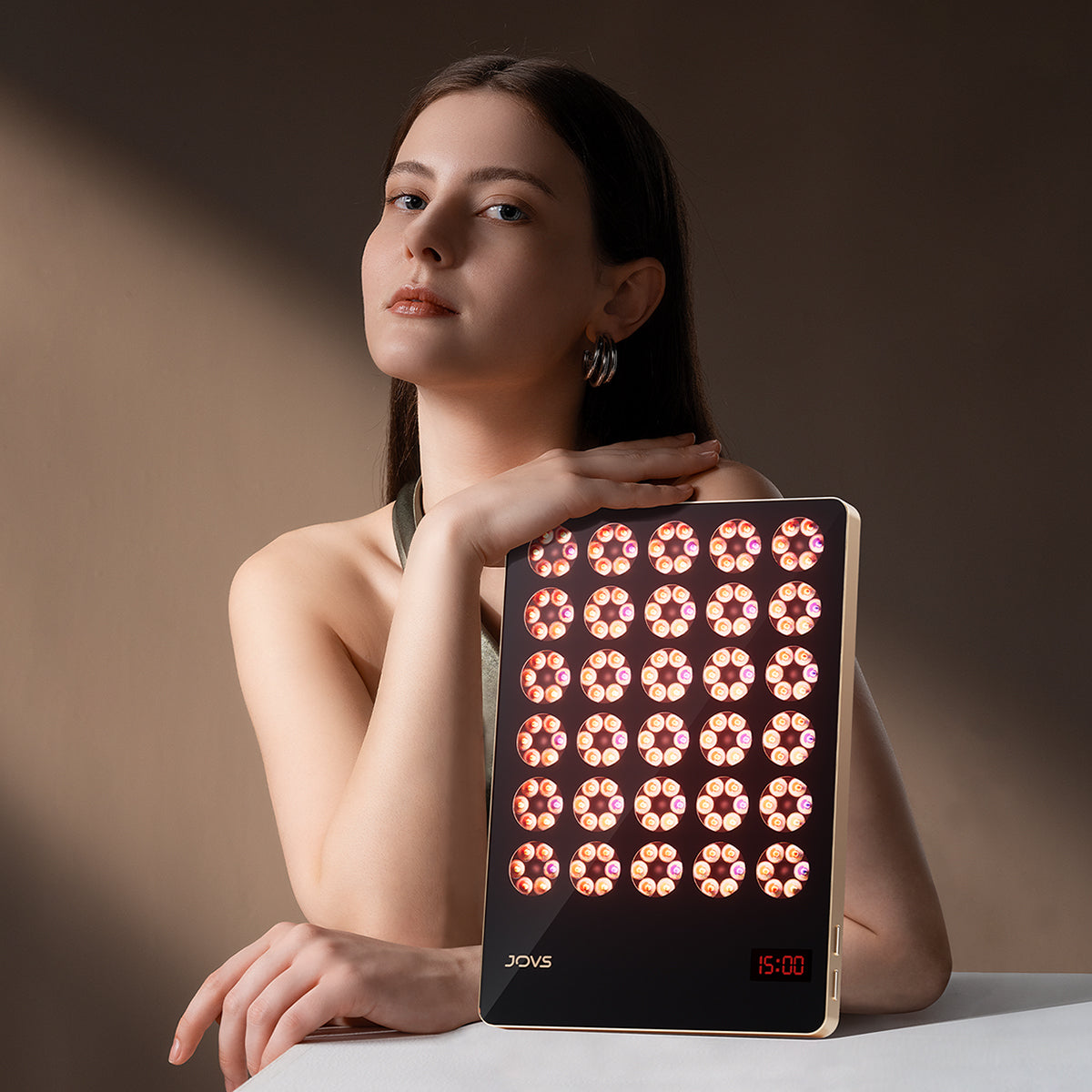 Elegant young woman with JOVS LED light therapy device promoting rejuvenation and skincare health.