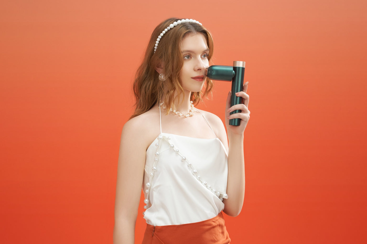 Elegant woman holding IPL hair removal device during beauty session on orange background