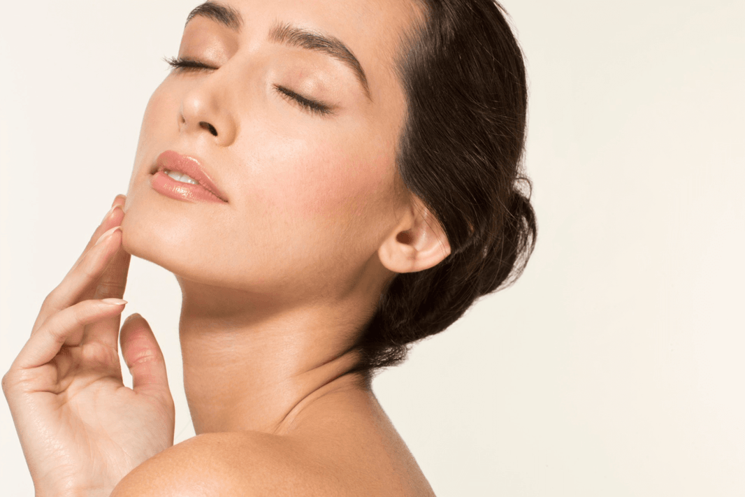 Close-up of a woman with glowing hydrated skin gently touching her face against a light background