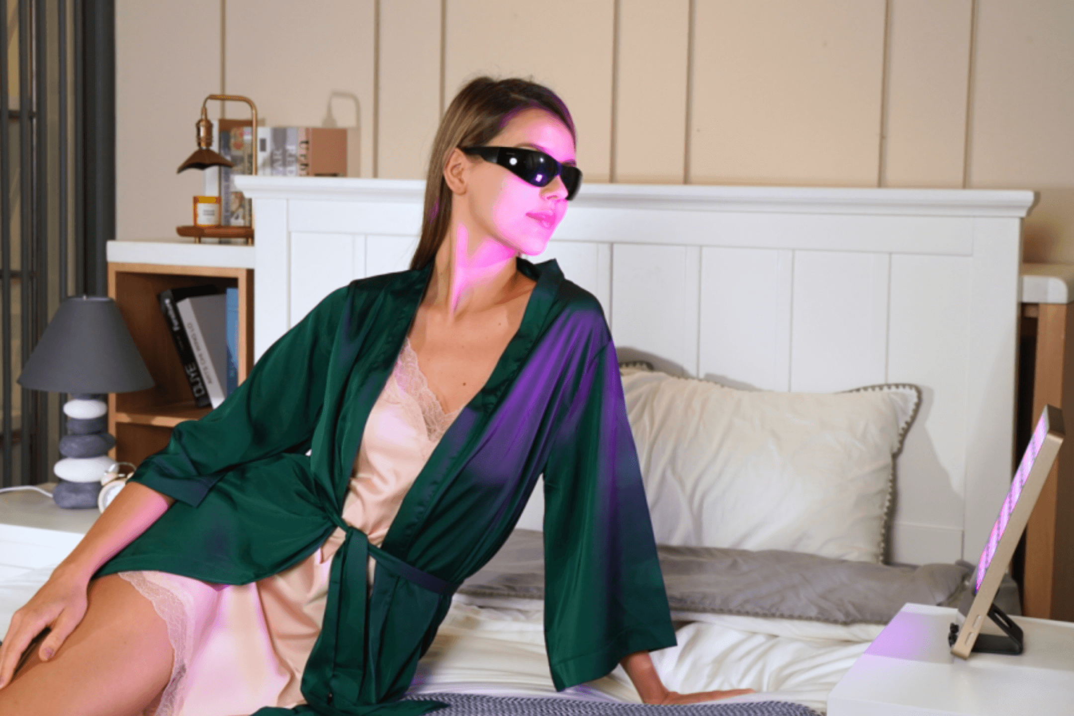 Woman using a red light therapy device while wearing a green robe and protective goggles