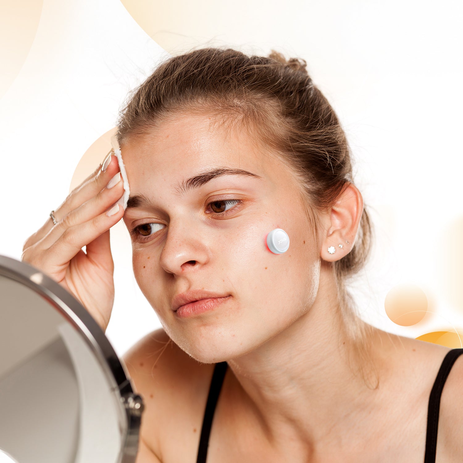 Young woman using JOVS LED skincare pimple patch for acne treatment.